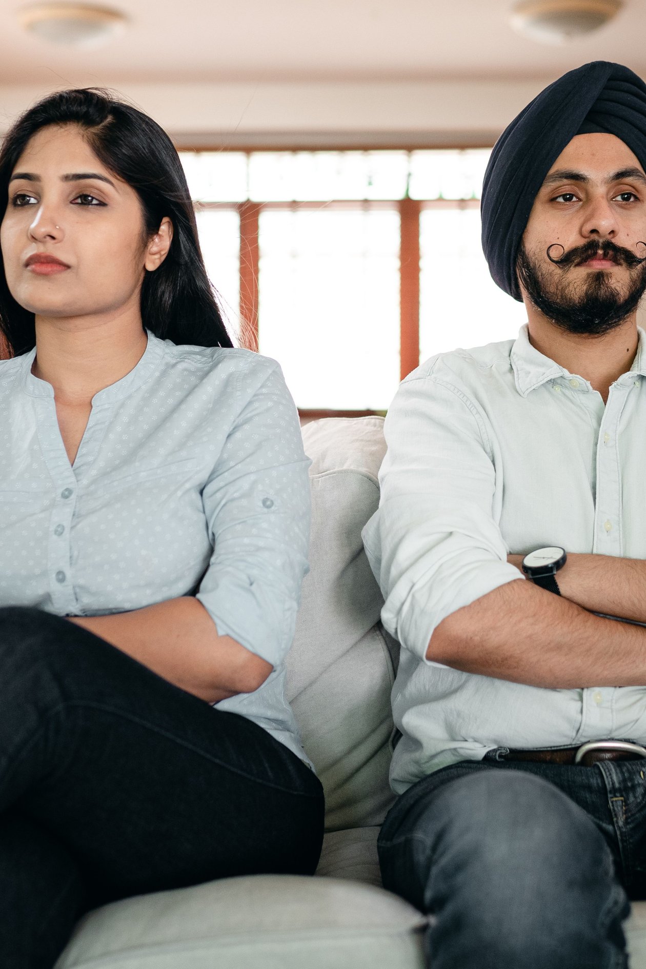 A couple sitting on a sofa with crossed arms, not looking at each other