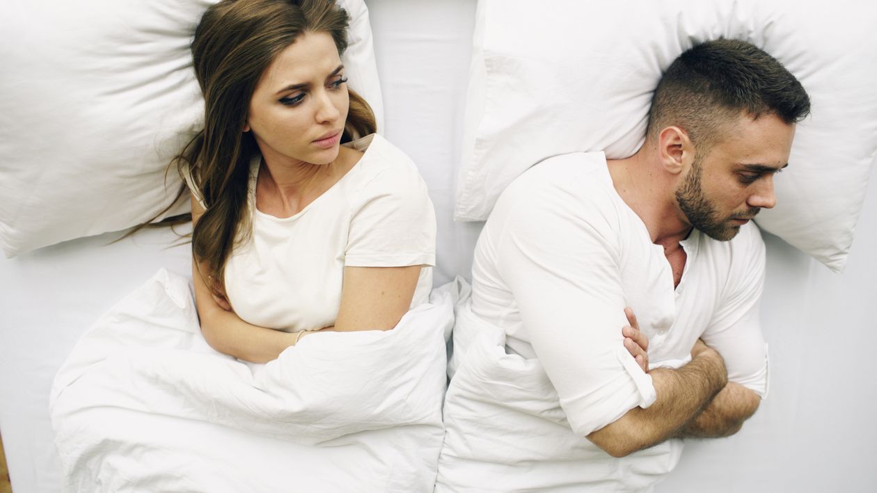A couple lying in bed facing away from each other, tense